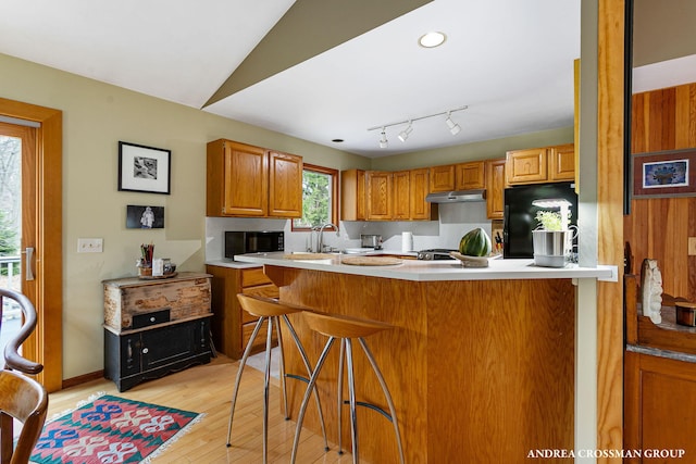 kitchen featuring light countertops, a kitchen bar, brown cabinets, light wood-type flooring, and black fridge