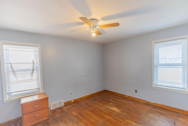 spare room with baseboards, ceiling fan, visible vents, and dark wood finished floors