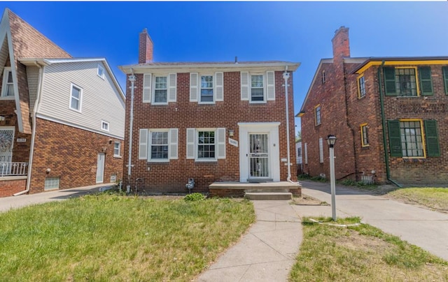 view of front of home with a front lawn, a chimney, and brick siding