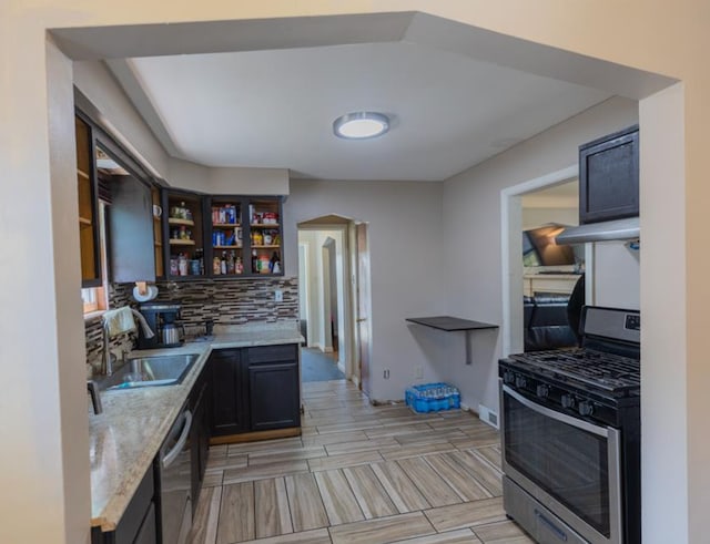 kitchen with a sink, open shelves, tasteful backsplash, light stone countertops, and appliances with stainless steel finishes
