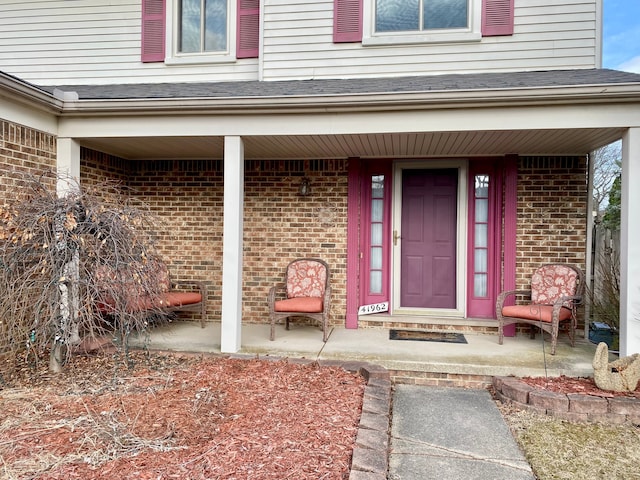 view of exterior entry with brick siding and covered porch