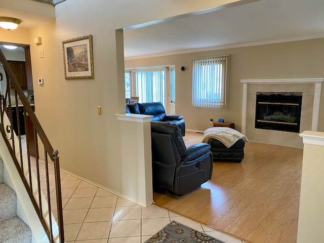 living room featuring light wood-type flooring, a tiled fireplace, baseboards, stairs, and crown molding