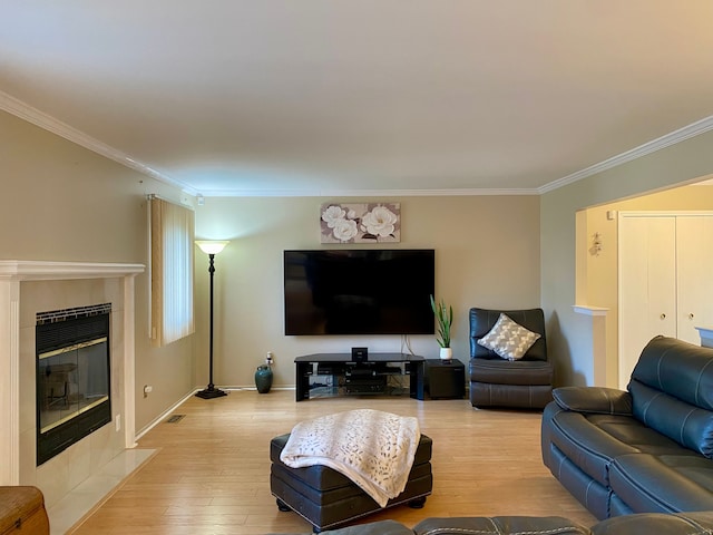 living room featuring a tiled fireplace, baseboards, light wood-style floors, and ornamental molding