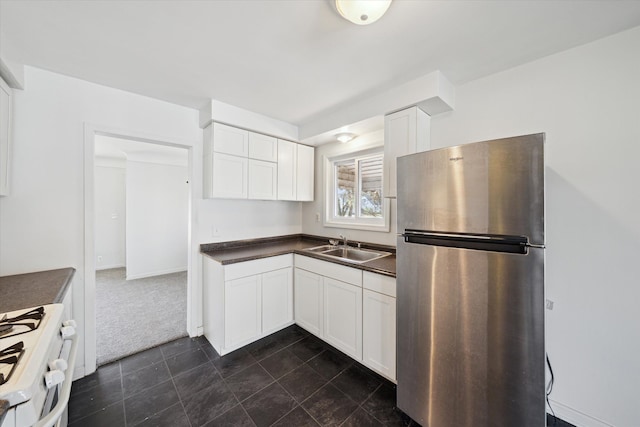 kitchen with white gas range oven, white cabinetry, freestanding refrigerator, dark countertops, and a sink