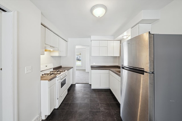 kitchen featuring white range with gas stovetop, white cabinets, freestanding refrigerator, and dark countertops