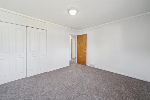unfurnished bedroom featuring visible vents, baseboards, a closet, ornamental molding, and carpet floors