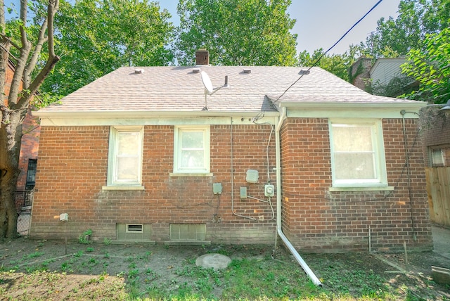 rear view of property featuring a chimney, brick siding, and a shingled roof