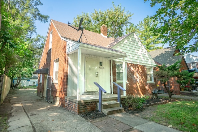 bungalow-style house featuring fence, roof with shingles, a chimney, and brick siding