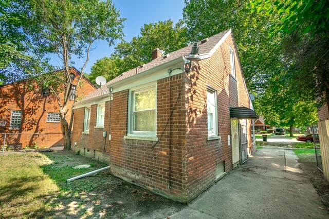 view of side of property with fence, roof with shingles, a chimney, and brick siding