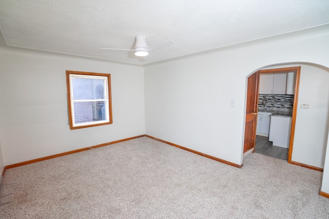 empty room with arched walkways, a ceiling fan, carpet floors, and baseboards