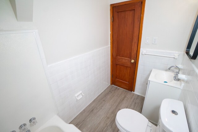 full bath featuring wood finished floors, tile walls, a wainscoted wall, toilet, and vanity