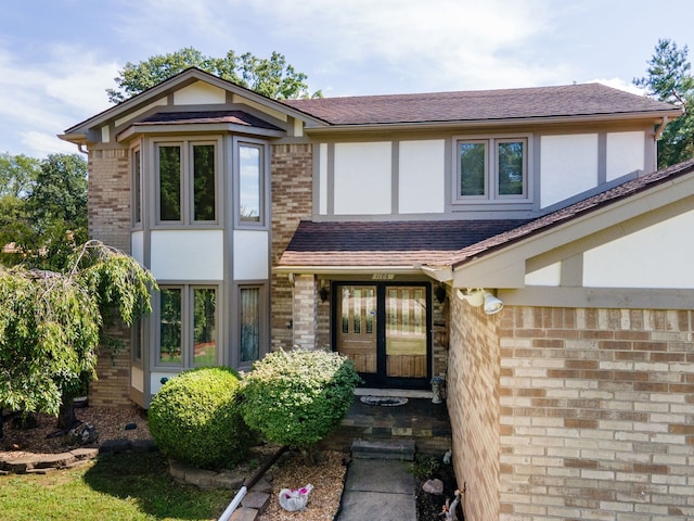 view of front of property with brick siding, roof with shingles, and stucco siding