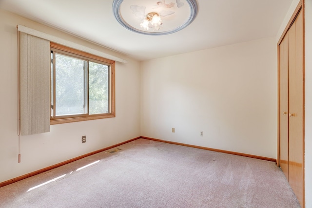 unfurnished bedroom featuring baseboards, light colored carpet, visible vents, and a closet