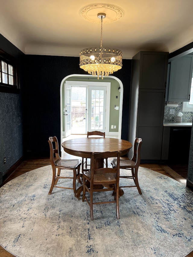 dining space with an inviting chandelier, arched walkways, baseboards, and wood finished floors