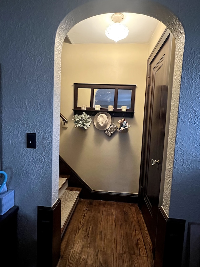 corridor with arched walkways, a textured wall, and wood finished floors
