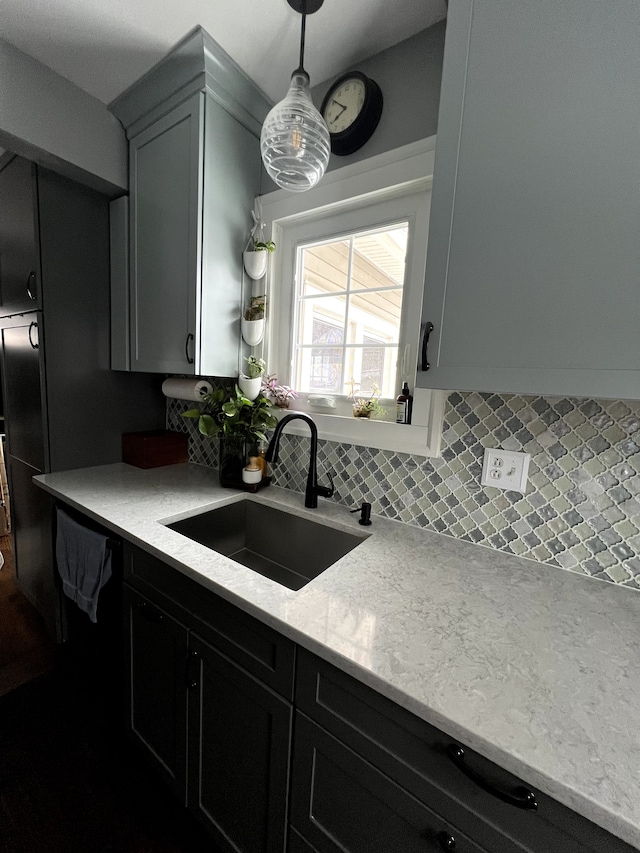 kitchen featuring decorative light fixtures, light stone countertops, a sink, and tasteful backsplash