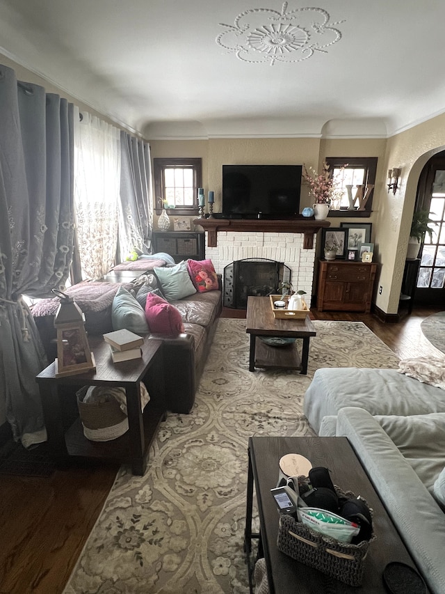 living area with arched walkways, ornamental molding, a fireplace, and wood finished floors