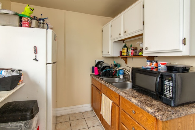 kitchen featuring freestanding refrigerator, black microwave, white cabinets, light tile patterned flooring, and a sink