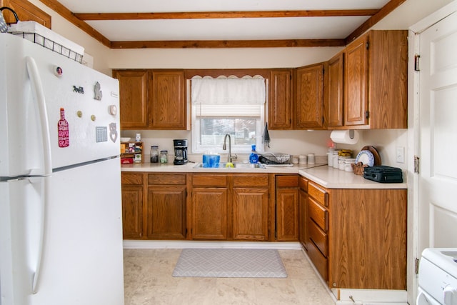 kitchen with light countertops, brown cabinets, a sink, and freestanding refrigerator