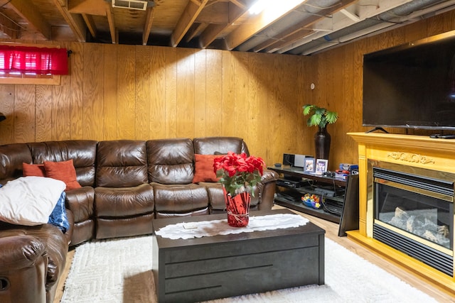 living area with visible vents, wooden walls, wood finished floors, and a glass covered fireplace