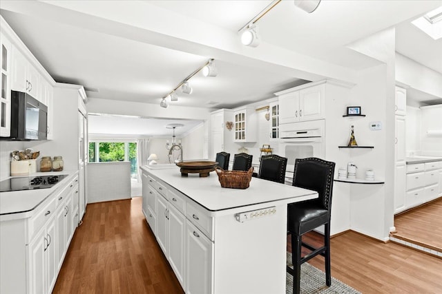 2865 Steeple Hill Rd, White Lake, MI 48383 - kitchen with black electric stovetop, a breakfast bar area, white cabinets, track lighting, and wood finished floors
