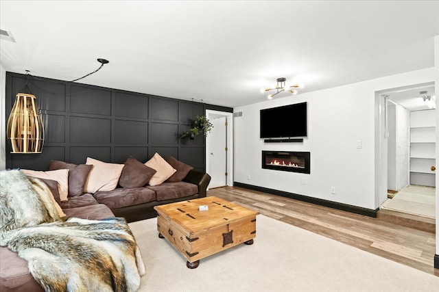 2865 Steeple Hill Rd, White Lake, MI 48383 - living room featuring a decorative wall, wood finished floors, a glass covered fireplace, a chandelier, and baseboards