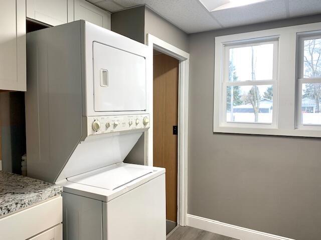 laundry area featuring stacked washer and clothes dryer, cabinet space, baseboards, and wood finished floors