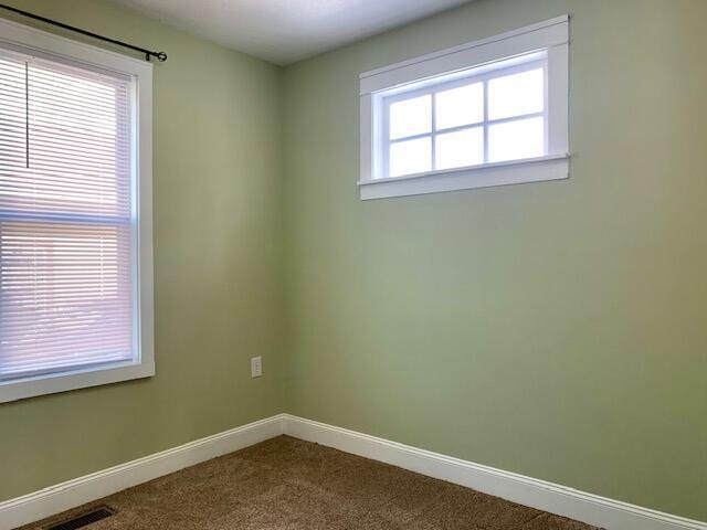 unfurnished room with baseboards, visible vents, and dark colored carpet
