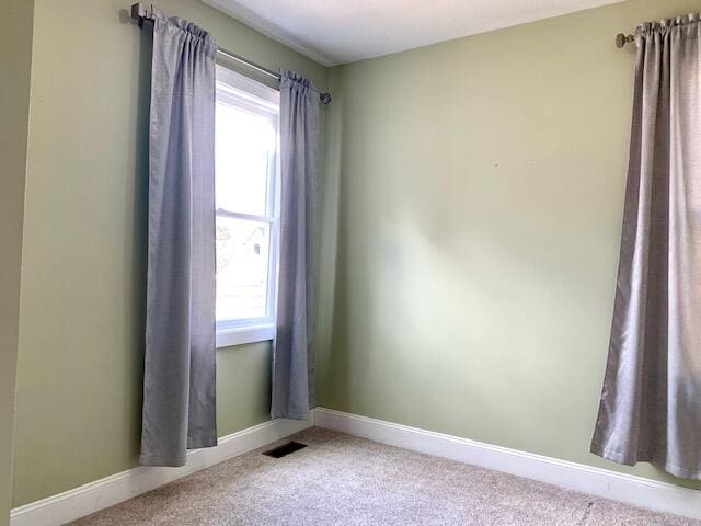 carpeted spare room featuring plenty of natural light, baseboards, and visible vents