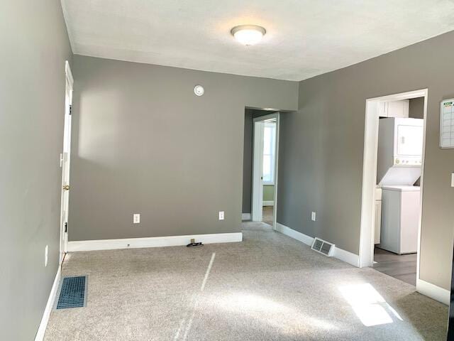 empty room with stacked washer and dryer, carpet flooring, visible vents, and baseboards
