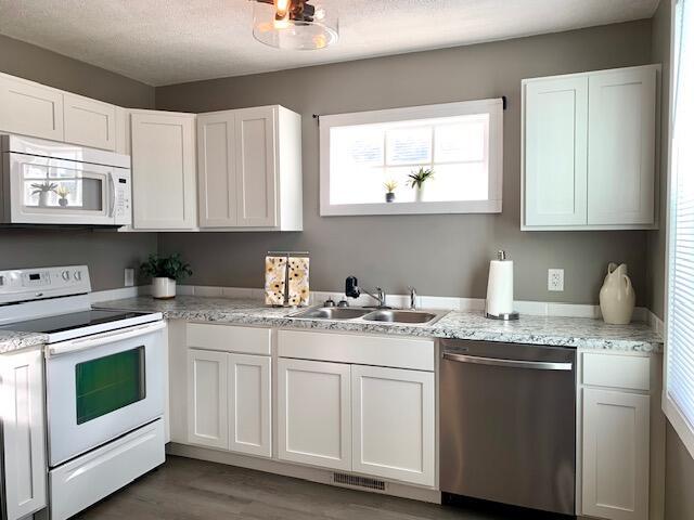 kitchen featuring white cabinetry, white appliances, a sink, visible vents, and wood finished floors