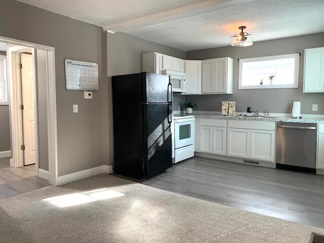 kitchen featuring white appliances, baseboards, white cabinetry, a sink, and light wood-type flooring