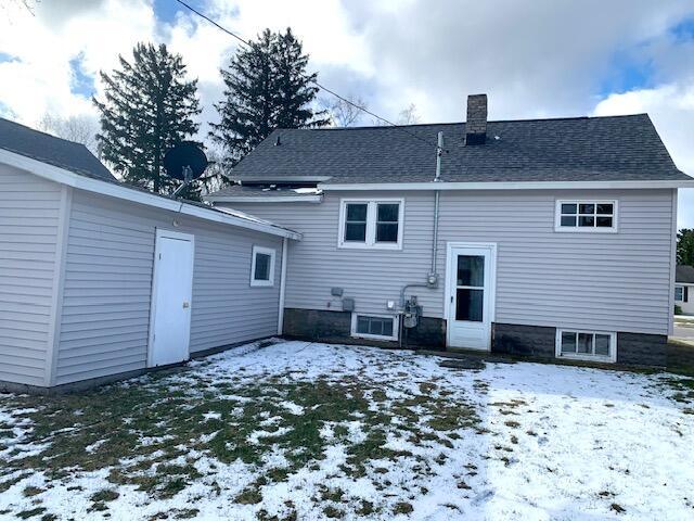 snow covered rear of property with roof with shingles and a chimney