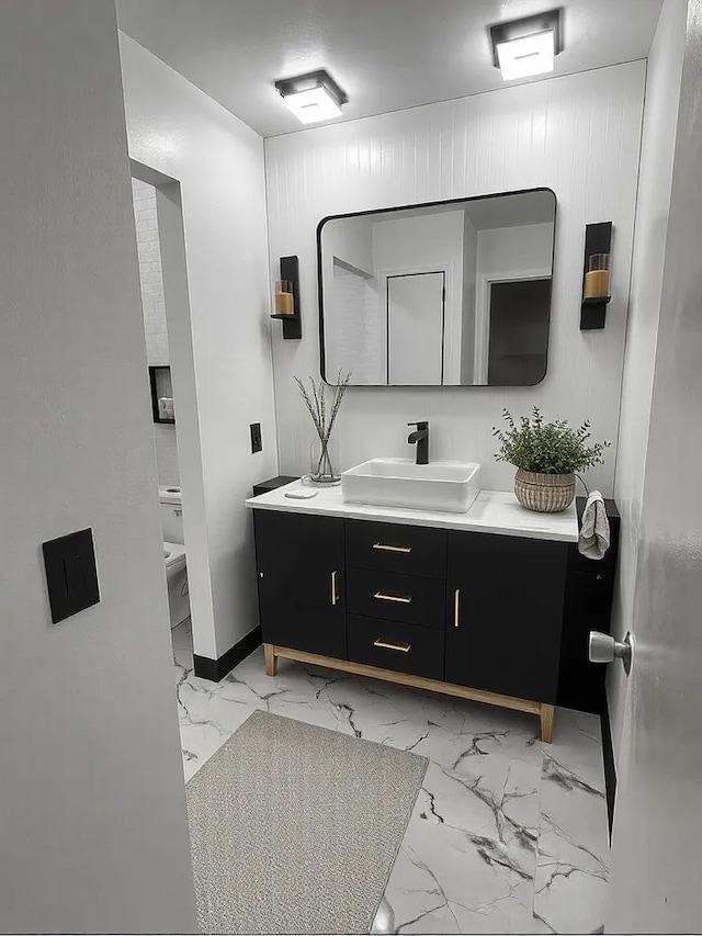 bathroom featuring toilet, baseboards, marble finish floor, and vanity