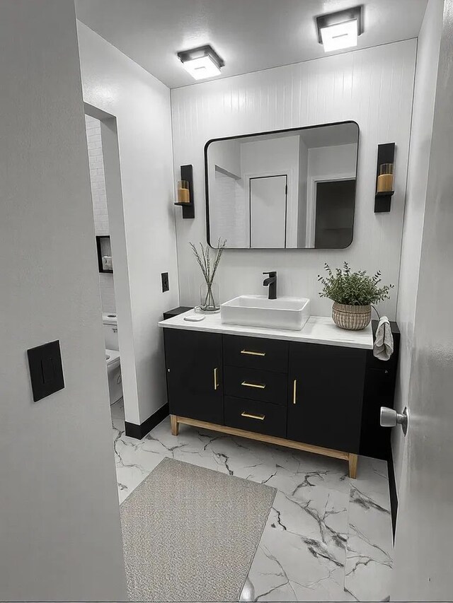 bathroom featuring vanity, marble look tile flooring, toilet, and baseboards