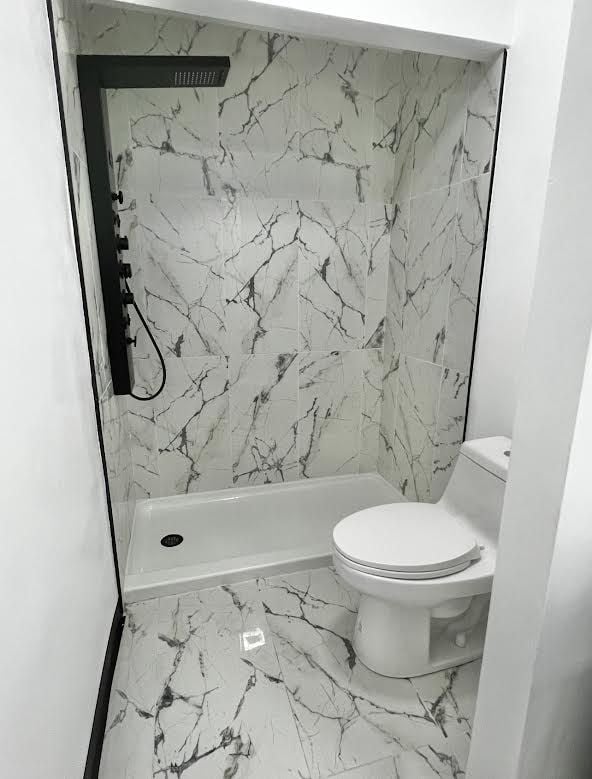 bathroom with marble look tiles, toilet, and a stall shower