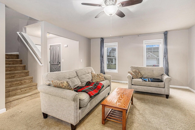 living room featuring baseboards, stairs, a ceiling fan, and light carpet