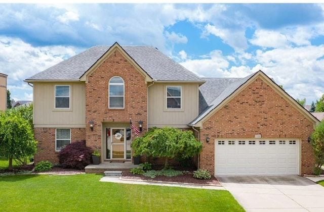 view of front of property featuring brick siding, a front yard, driveway, and a garage