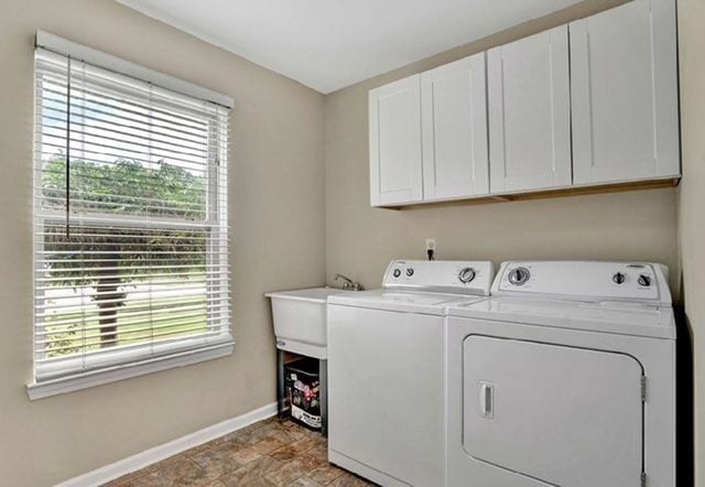 washroom featuring stone finish floor, baseboards, washing machine and dryer, and cabinet space