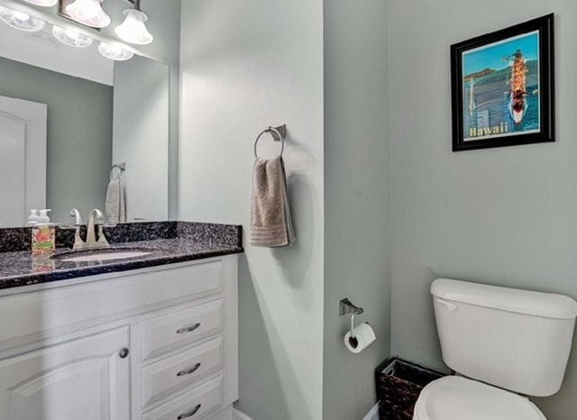 half bath featuring baseboards, toilet, and vanity