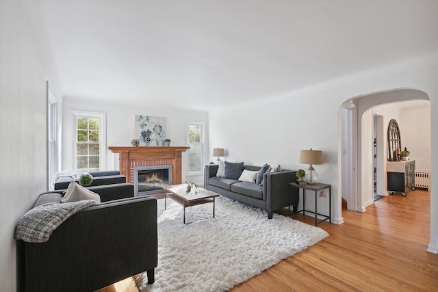 21124 Thorofare Rd, Grosse Ile, MI 48138 - living room featuring light wood finished floors, a brick fireplace, arched walkways, and radiator