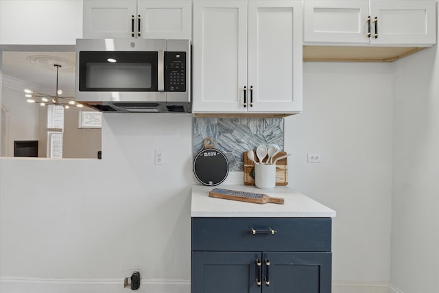5784 Whittier St, Detroit, MI 48224 - kitchen featuring decorative backsplash, a chandelier, stainless steel microwave, light countertops, and white cabinets