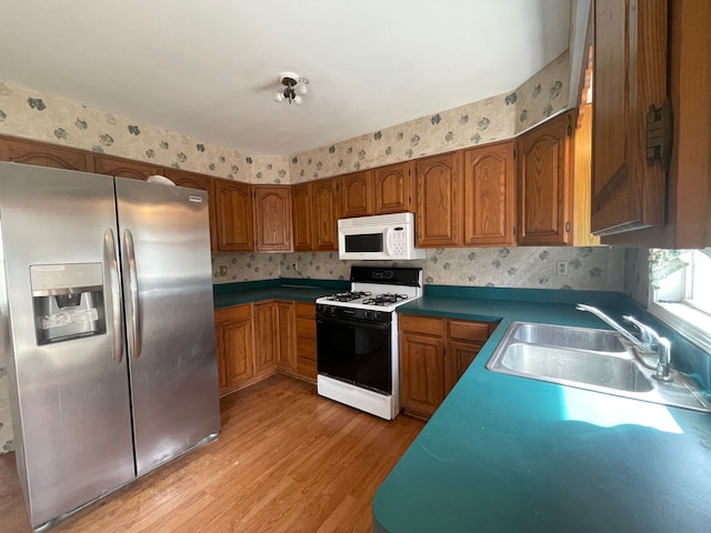 kitchen with stainless steel fridge, a sink, light wood-style floors, white microwave, and range with gas cooktop