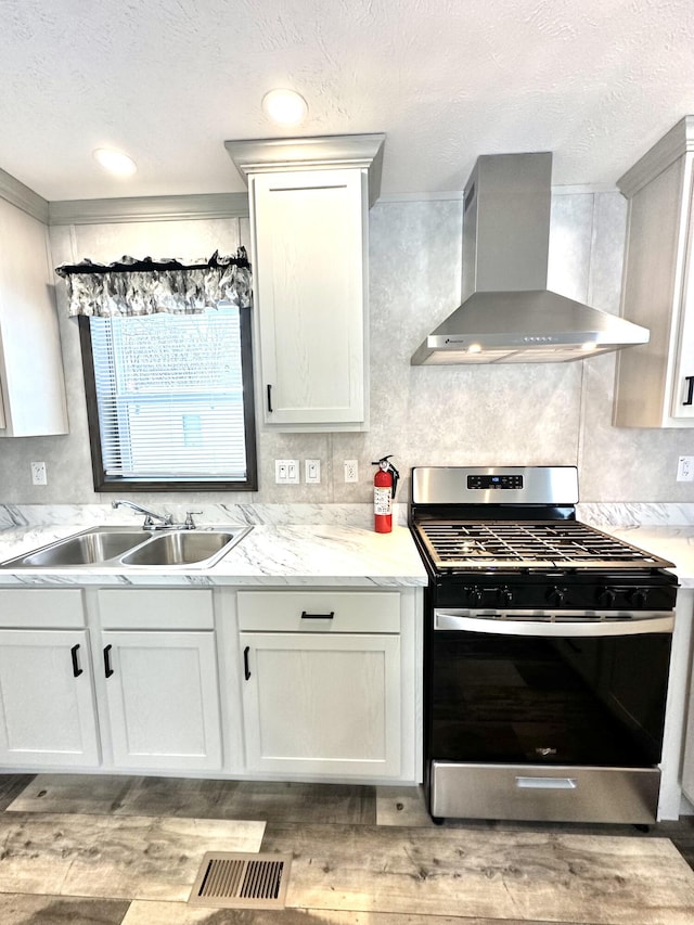 3502 Beech Ln, Twin Lake, MI 49457 - kitchen with wall chimney range hood, gas stove, light wood-style floors, a textured ceiling, and white cabinets