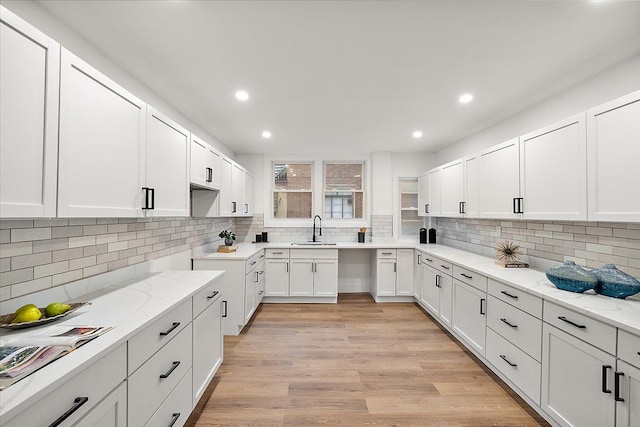 kitchen featuring a sink, decorative backsplash, light wood-style floors, and light stone countertops