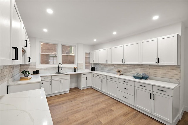 kitchen featuring tasteful backsplash, white cabinets, light stone counters, a sink, and light wood finished floors