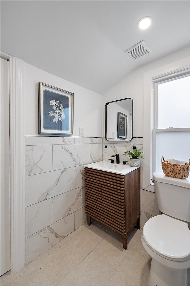 bathroom featuring vanity, visible vents, toilet, lofted ceiling, and tile walls