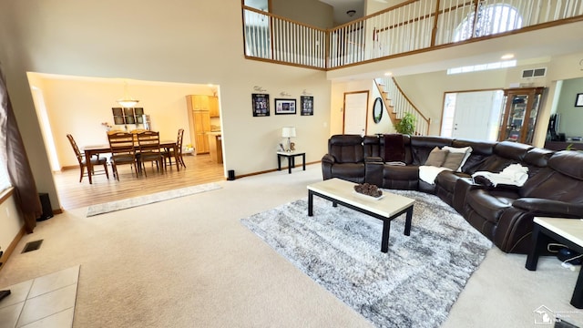 carpeted living area featuring baseboards, a towering ceiling, and visible vents