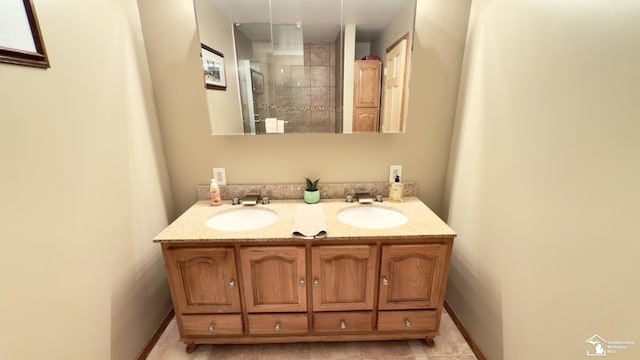 full bath featuring baseboards, double vanity, a sink, and tiled shower