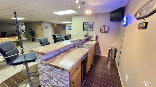 bar with baseboards, a drop ceiling, a sink, dishwashing machine, and indoor wet bar